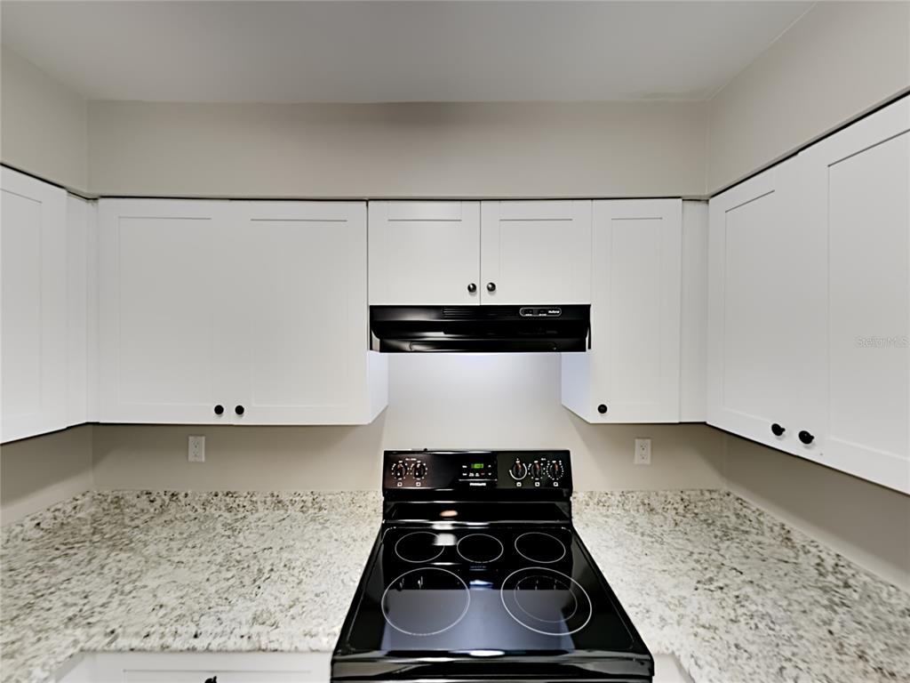 A kitchen features white cabinets, a black stove, and speckled granite countertops — 4128 SUNNY LAND DRIVE, LAKELAND, FL