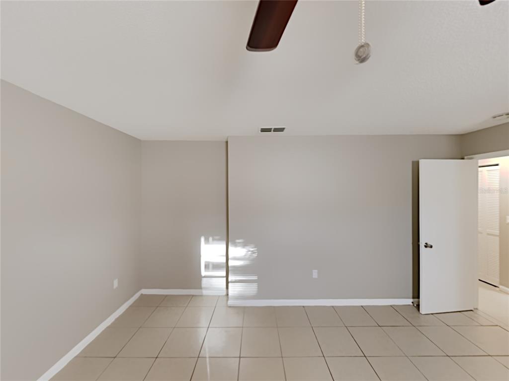An empty room features light-colored tile flooring, beige walls, and a ceiling fan — 4128 SUNNY LAND DRIVE, LAKELAND, FL