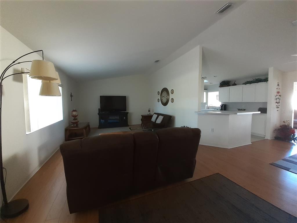 A living room with wood-look flooring opens to a kitchen with white cabinets and counters — 11655 SW 140TH LANE, DUNNELLON, FL