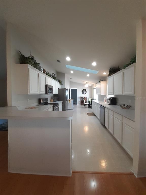 A galley-style kitchen features white cabinets, laminate countertops, and a skylight in the vaulted ceiling — 11655 SW 140TH LANE, DUNNELLON, FL