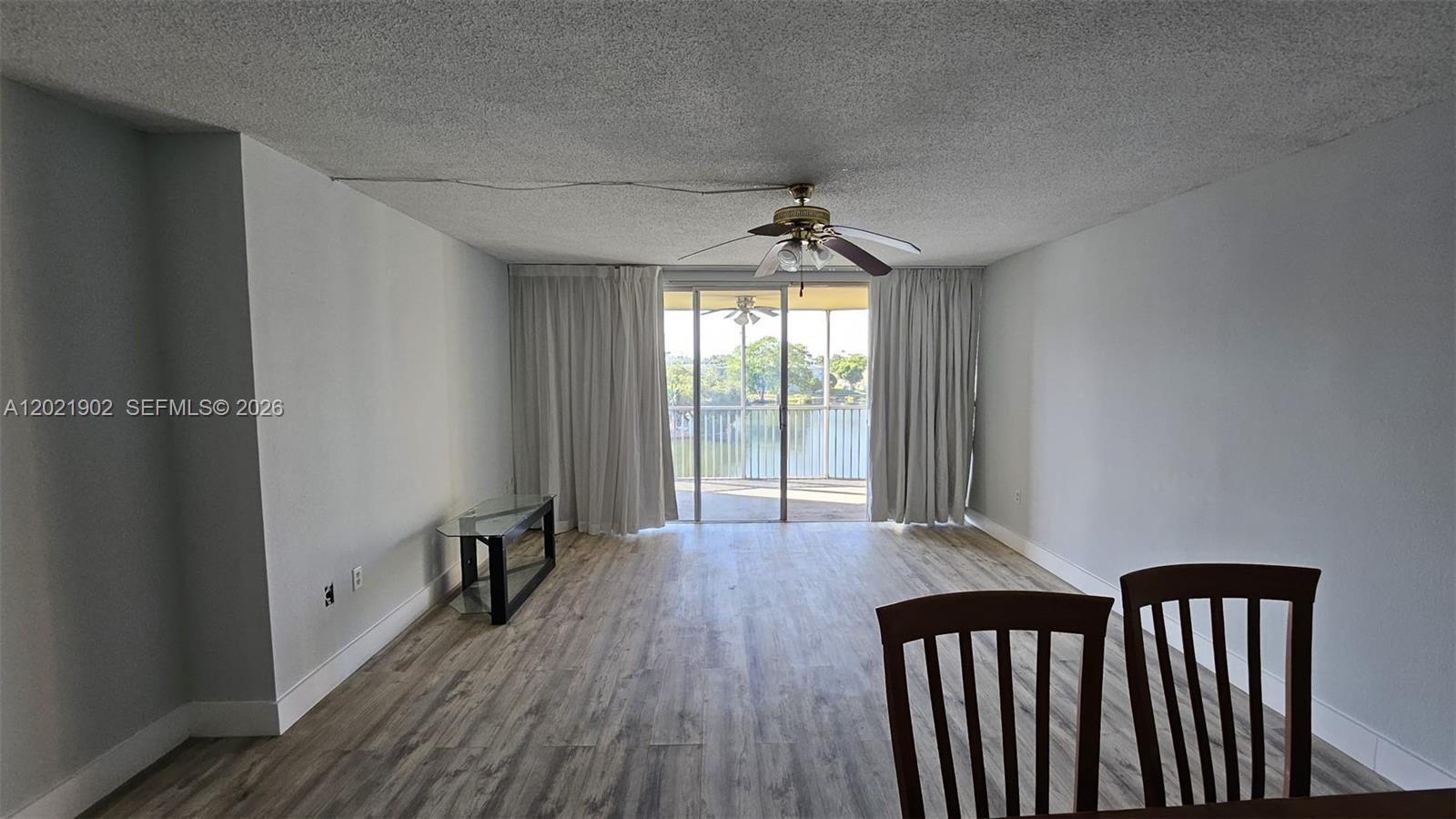 A living room with wood-look flooring, a ceiling fan, and a sliding door to a balcony — 1750 NE 191st St # 4, Miami FL 33179, MIAMI, FL
