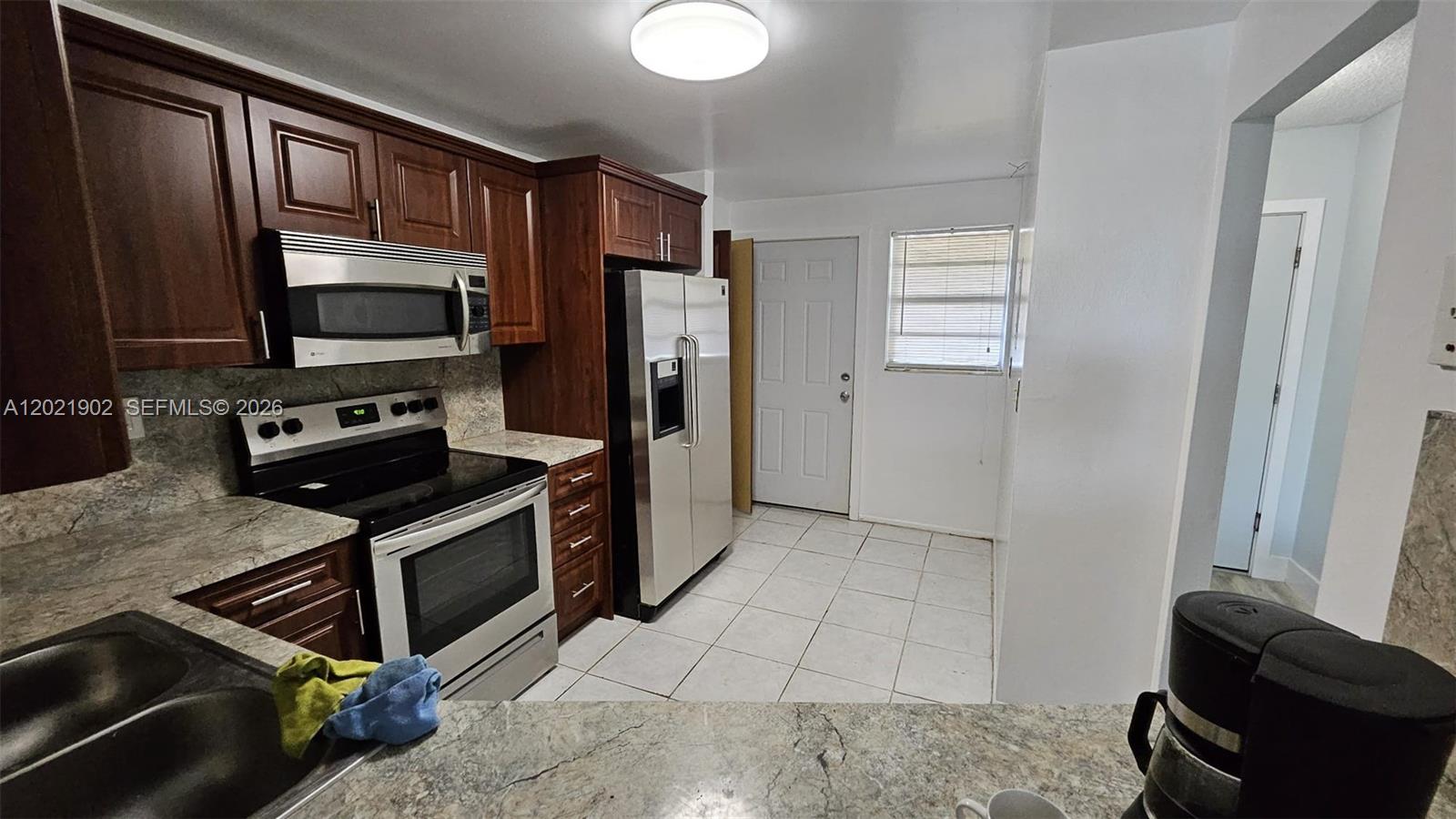 A kitchen features dark wood cabinets, stainless steel appliances, and light-colored tile flooring — 1750 NE 191st St # 4, Miami FL 33179, MIAMI, FL