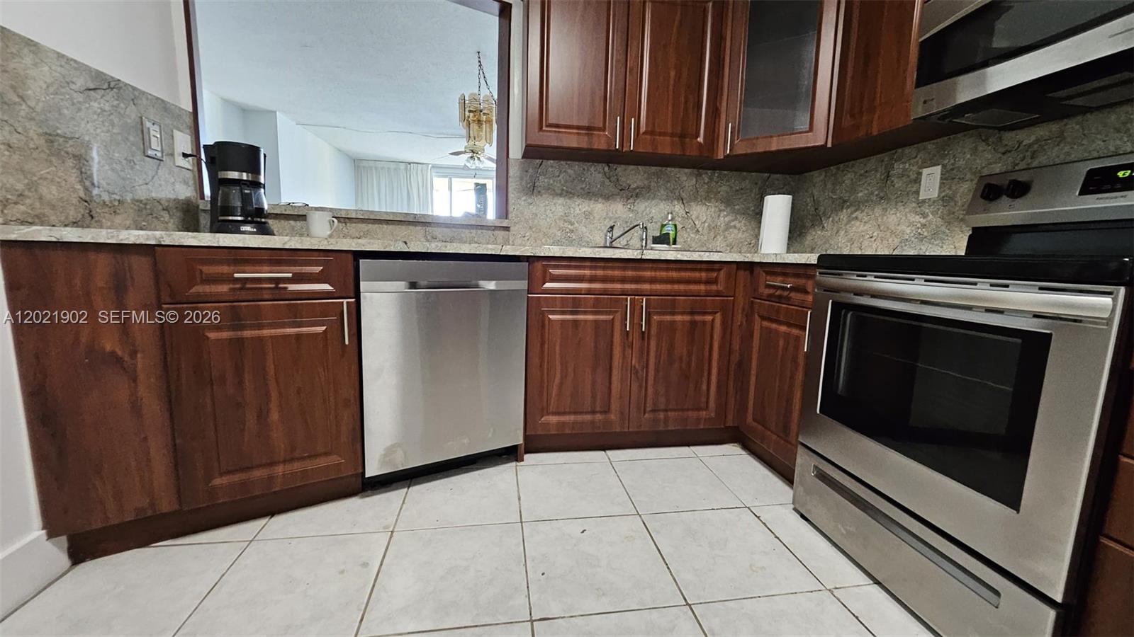 A kitchen features wood cabinets, stainless steel appliances, and a pass-through window to another room — 1750 NE 191st St # 4, Miami FL 33179, MIAMI, FL