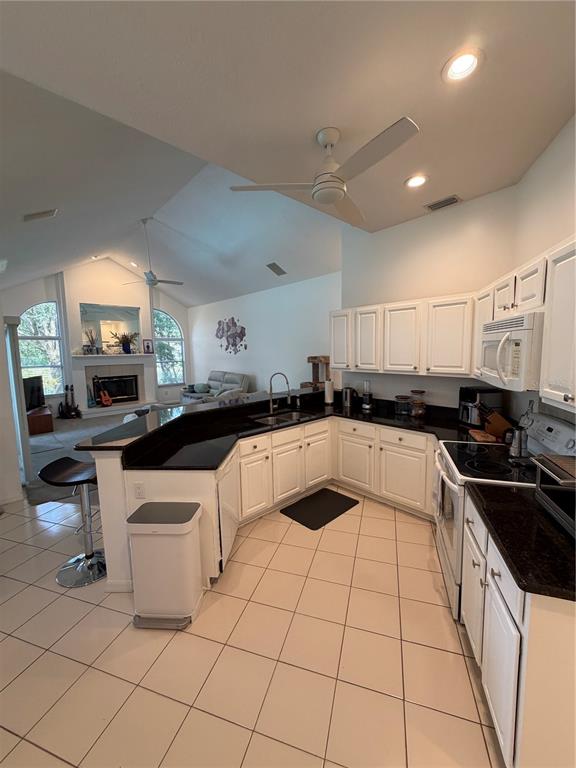 A kitchen with white cabinets and black countertops overlooks a living room with a fireplace — 2435 SWEETWATER COUNTRY CLUB PLACE DRIVE, APOPKA, FL