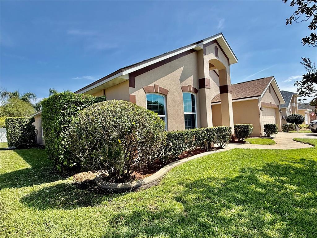 A tan house with a brown roof and arched windows sits behind a manicured hedge — 1115 PROSPERITY AVENUE, KISSIMMEE, FL