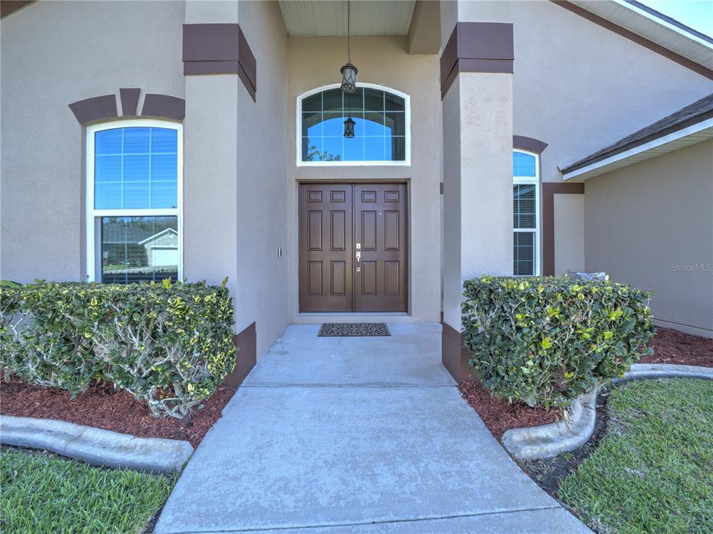 A concrete walkway leads to the double front doors of a tan stucco house — 1115 PROSPERITY AVENUE, KISSIMMEE, FL