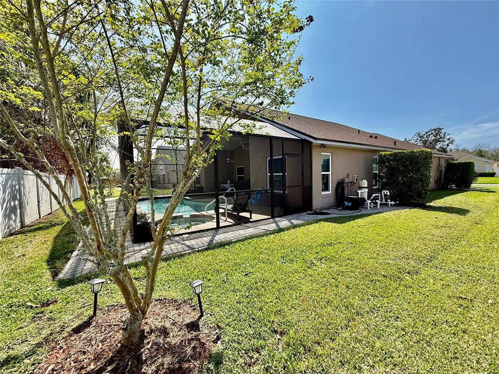 A backyard features a screened-in pool and patio area next to a tan house — 1115 PROSPERITY AVENUE, KISSIMMEE, FL