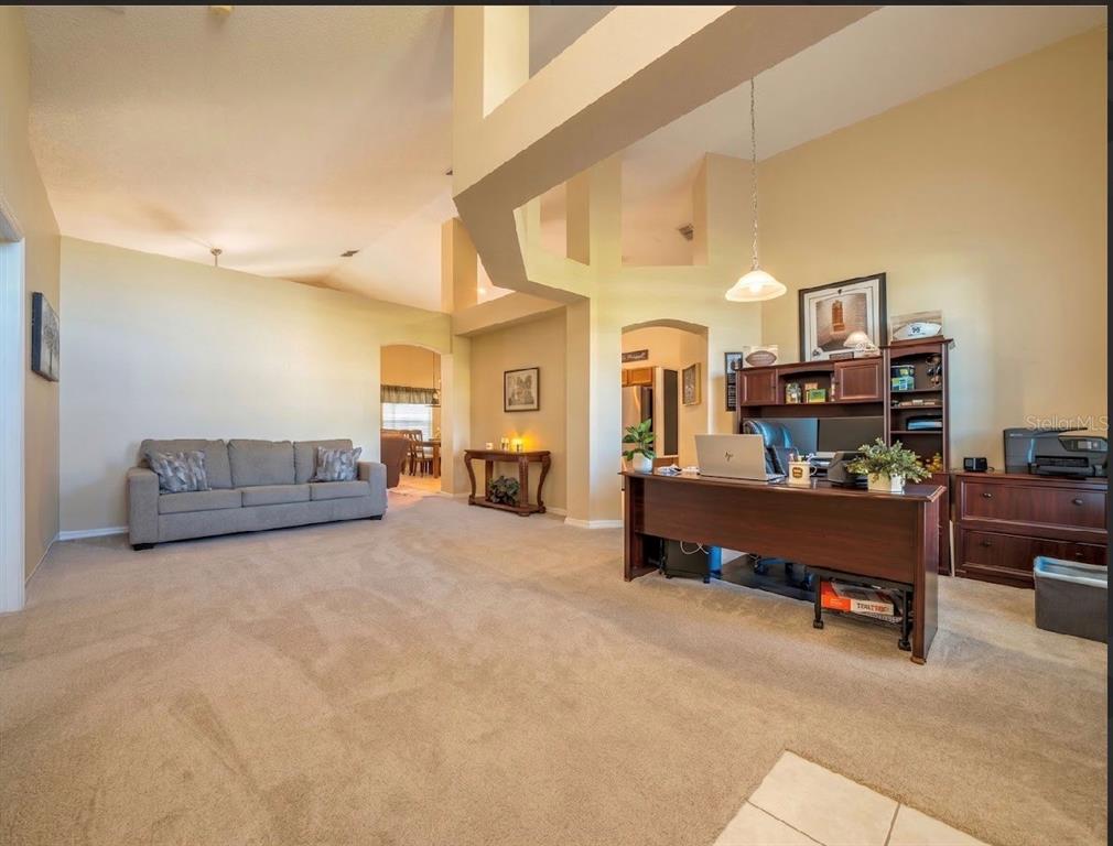 A spacious room features a gray sofa, a wooden desk, and high vaulted ceilings — 1115 PROSPERITY AVENUE, KISSIMMEE, FL