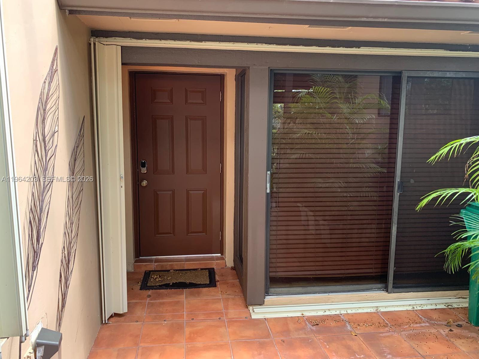 A brown front door sits next to a sliding glass door on a tiled patio — 3340 Torremolinos Ave # 40, Doral FL 33178, DORAL, FL