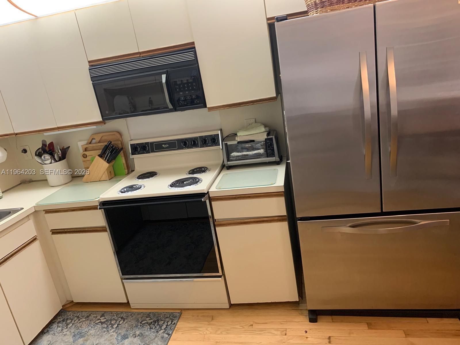 A kitchen features white cabinets, a black microwave, a white electric stove, and stainless refrigerator — 3340 Torremolinos Ave # 40, Doral FL 33178, DORAL, FL
