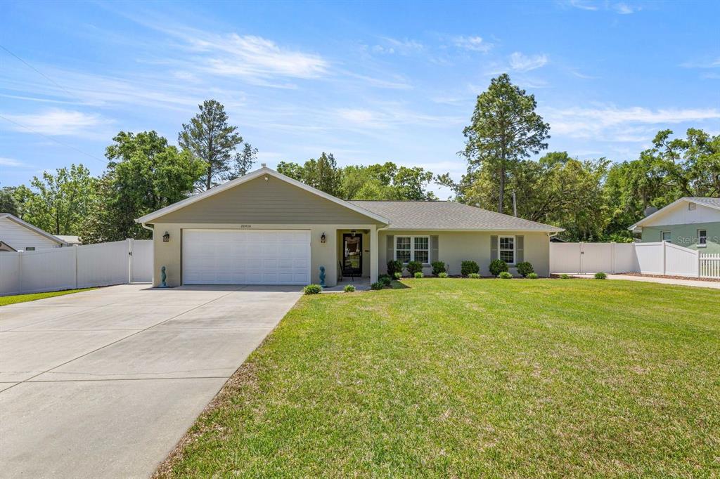 A single-story house with a two-car garage, light-colored siding, and a large front lawn — 20430 SW 80TH PLACE ROAD, DUNNELLON, FL