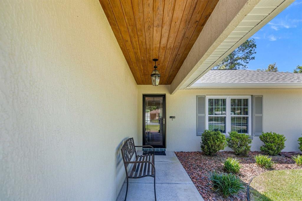 A covered front porch features a wood-paneled ceiling, a metal bench, and a glass door — 20430 SW 80TH PLACE ROAD, DUNNELLON, FL