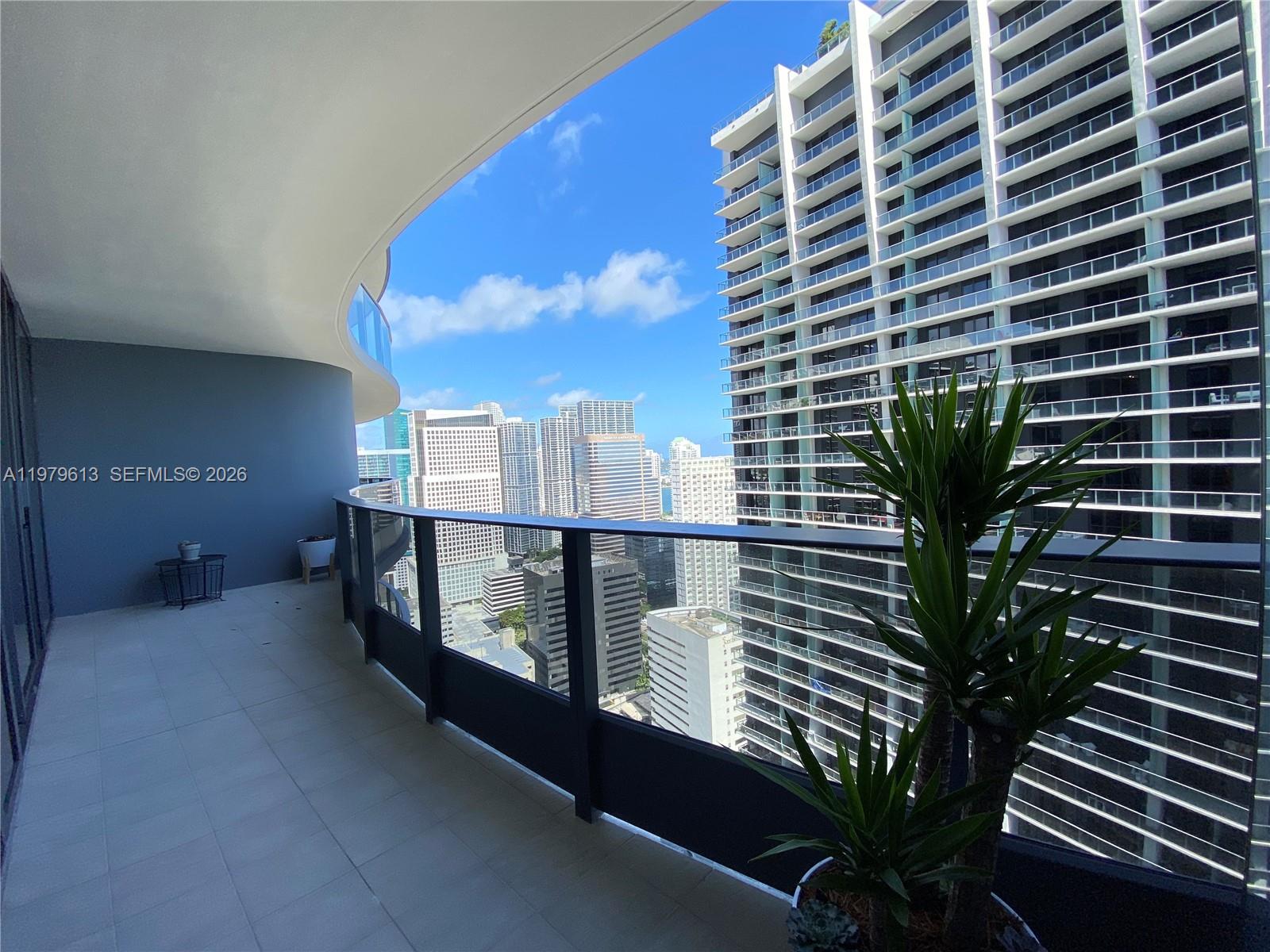 A curved balcony overlooks a city skyline with a tall residential building nearby — 1000 Brickell Plaza # 3807, Miami FL 33131, MIAMI, FL