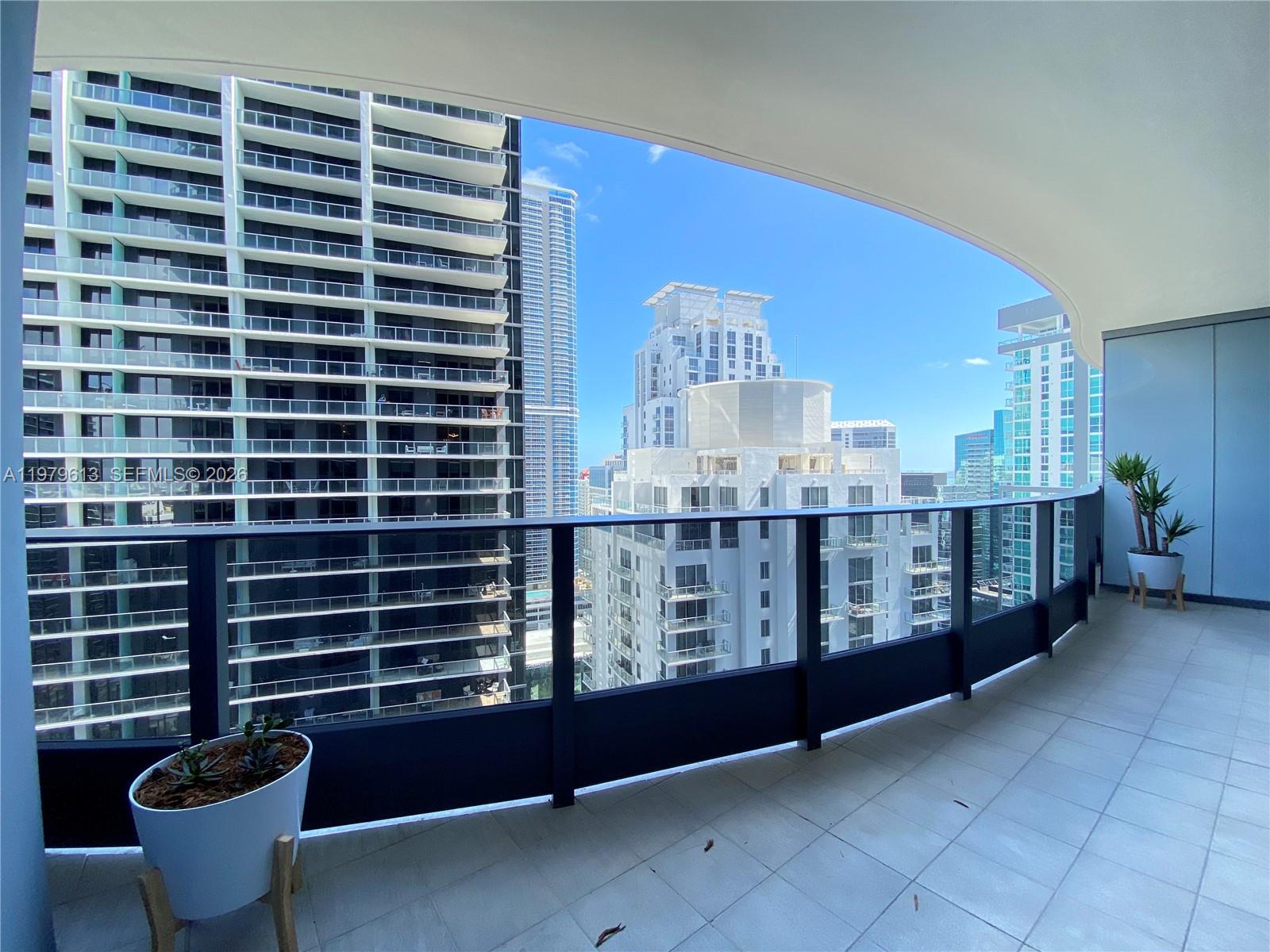 A curved balcony with a glass railing overlooks a dense urban skyline of high-rise buildings — 1000 Brickell Plaza # 3807, Miami FL 33131, MIAMI, FL