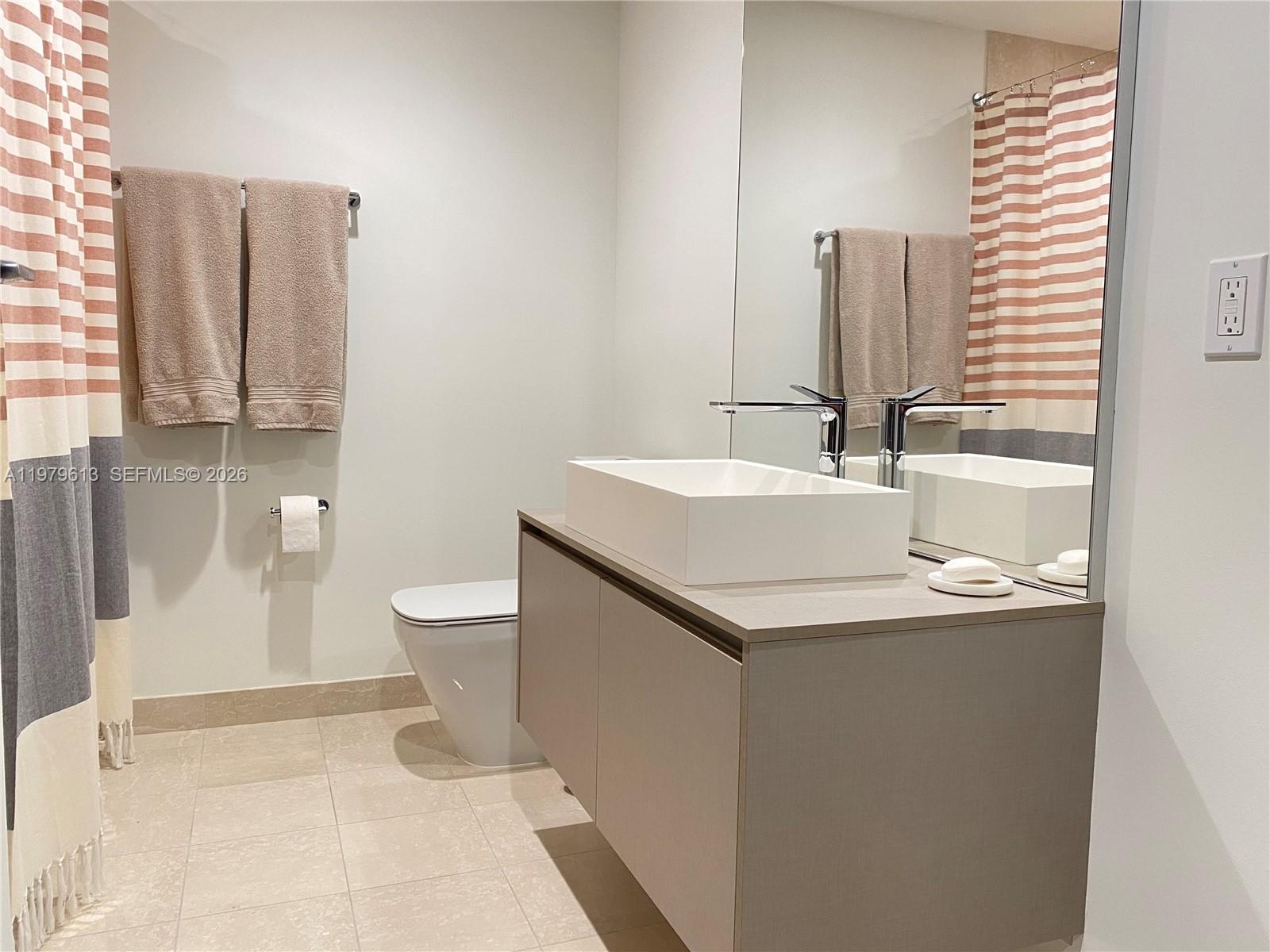 A modern bathroom features a floating vanity, vessel sink, and a striped shower curtain — 1000 Brickell Plaza # 3807, Miami FL 33131, MIAMI, FL