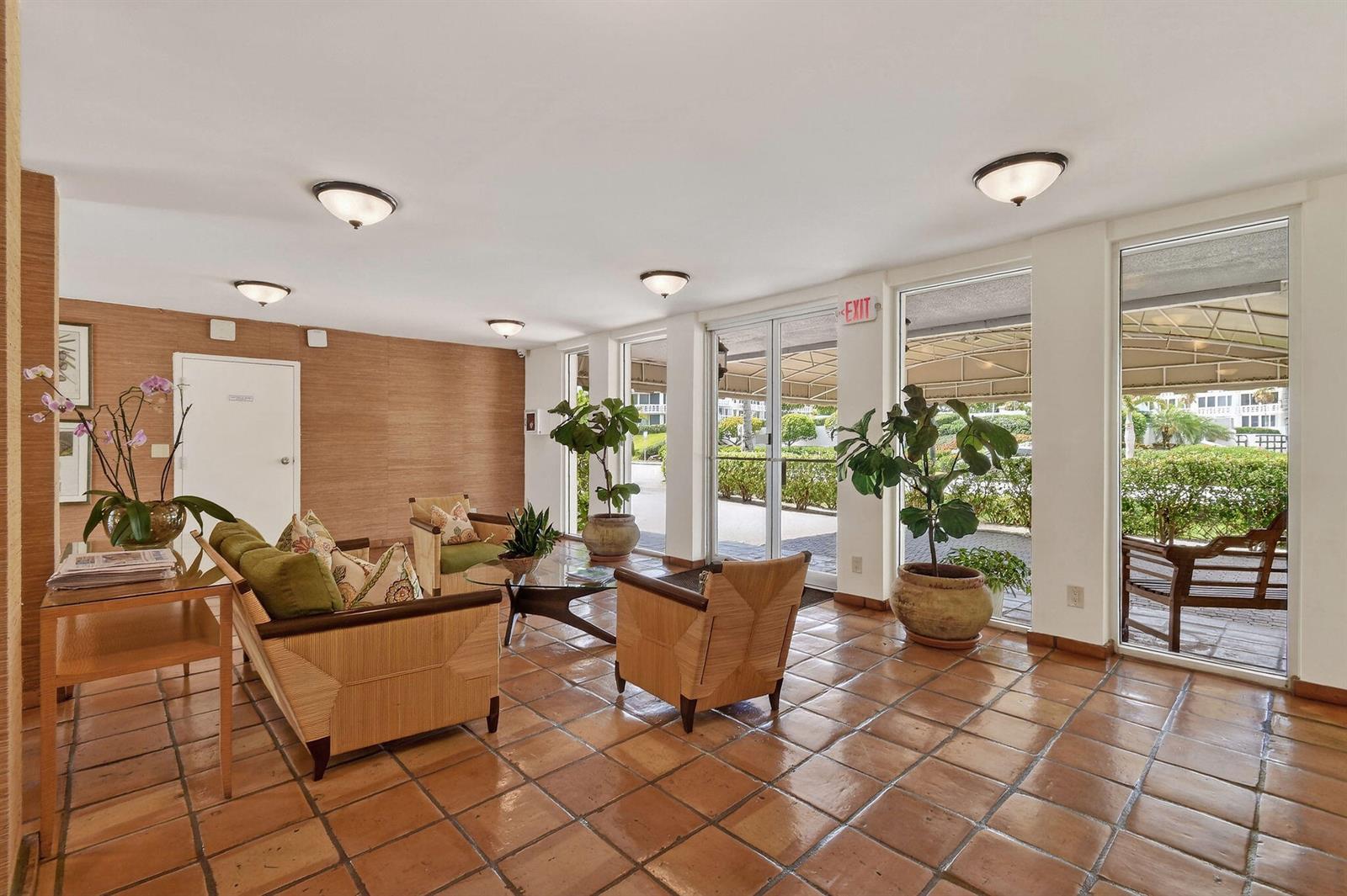A lobby with terracotta tile floors, wood-paneled walls, seating, and large windows overlooking a patio — 139 Sunrise Avenue # 2030, Palm Beach FL 33480, PALM BEACH, FL