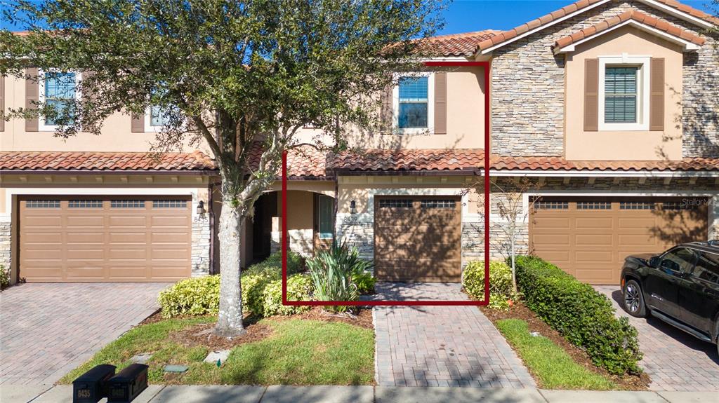 A two-story townhouse exterior features a brown garage door, stone accents, and a tiled roof — 8439 KELSALL DRIVE, ORLANDO, FL