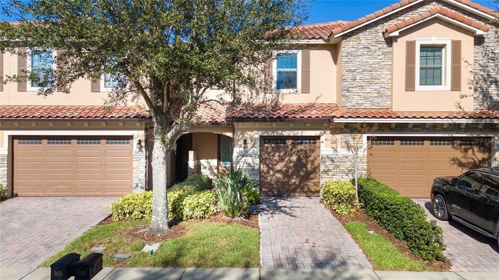 A row of three townhomes with beige stucco, stone accents, and brown garage doors — 8439 KELSALL DRIVE, ORLANDO, FL