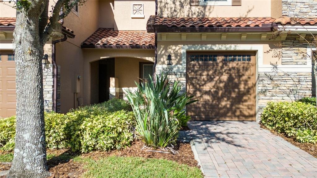 A residential building exterior features a brown garage door, stone accents, and a paved driveway — 8439 KELSALL DRIVE, ORLANDO, FL