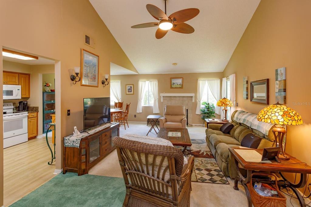 A living room with a vaulted ceiling, fireplace, ceiling fan, and adjacent kitchen area — 5301 WHITE CLIFF LANE UNIT 7, ORLANDO, FL