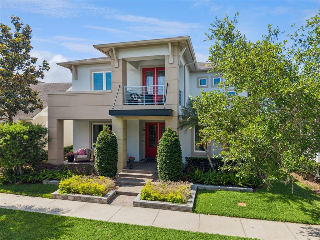 A two-story house features a red front door, a second-story balcony, and landscaped front gardens — 7974 GREENGARD STREET, ORLANDO, FL