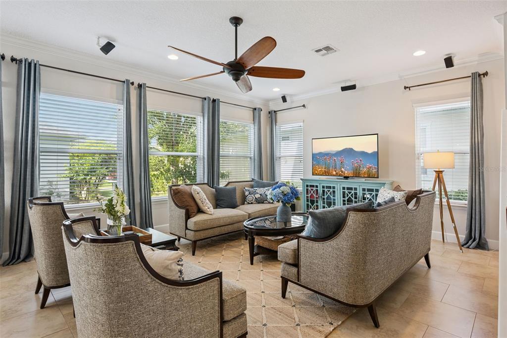A living room features a ceiling fan, neutral furniture, a television, and large windows with curtains — 7974 GREENGARD STREET, ORLANDO, FL