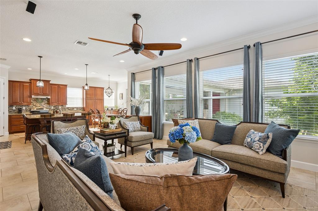 A living room with a ceiling fan, sofa, armchairs, and an open kitchen in the background — 7974 GREENGARD STREET, ORLANDO, FL