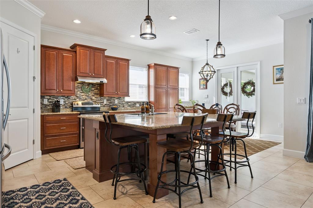 A kitchen with wood cabinets, granite countertops, a large island with stools, and tile flooring — 7974 GREENGARD STREET, ORLANDO, FL