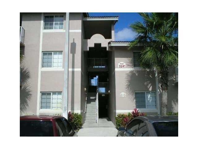 A three-story apartment building exterior with a central stairwell and parked cars in front — 3241 Sabal Palm Manor # 104, Davie FL 33024, DAVIE, FL