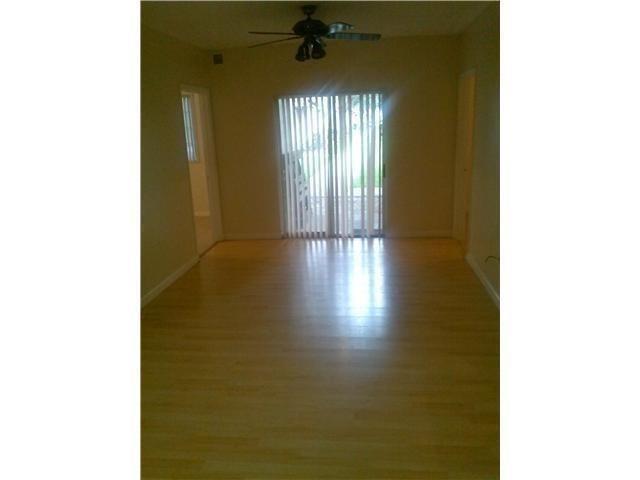 An empty room with light wood flooring, a ceiling fan, and vertical blinds on sliding doors — 3241 Sabal Palm Manor # 104, Davie FL 33024, DAVIE, FL