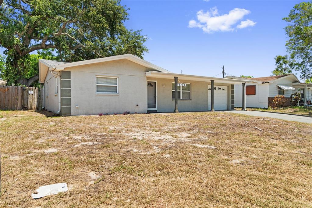 A single-story house with a beige stucco exterior, a covered porch, and a dry lawn — 3438 KIMBERLY OAKS DRIVE, HOLIDAY, FL