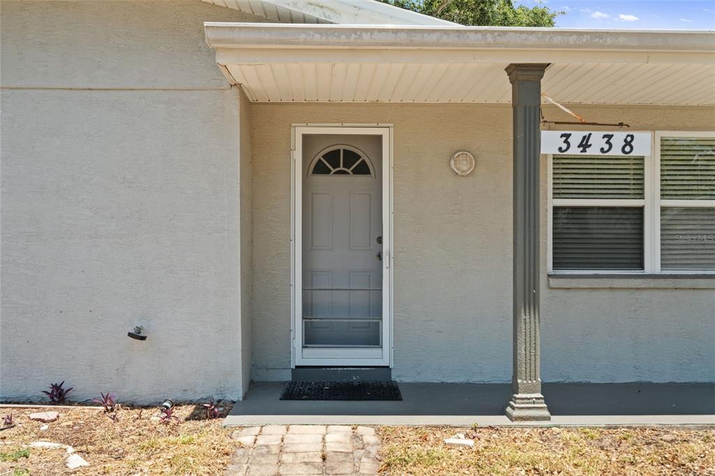 A front exterior view shows a beige house with a grey door and house numbers — 3438 KIMBERLY OAKS DRIVE, HOLIDAY, FL
