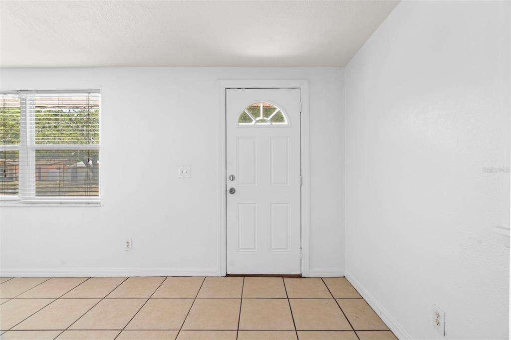 A room with white walls, tan tile flooring, a window with blinds, and a white door — 3438 KIMBERLY OAKS DRIVE, HOLIDAY, FL