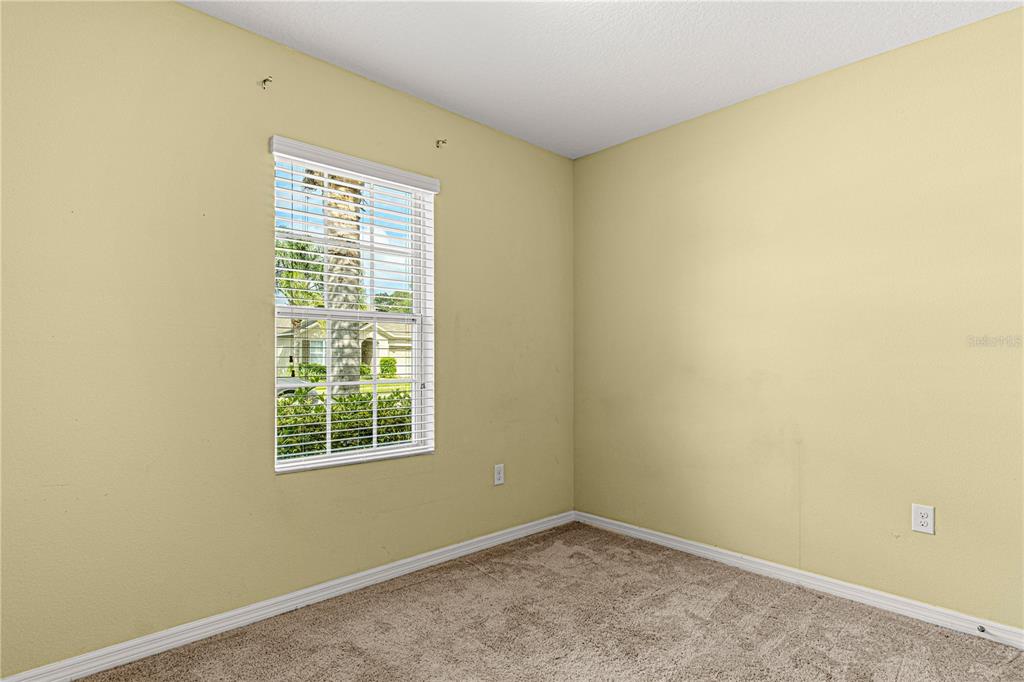 A corner of an empty bedroom with beige walls, tan carpeting, and a single window — 118 FISHERMANS COVE DRIVE, EDGEWATER, FL