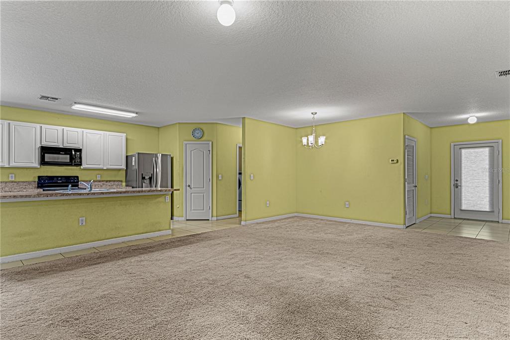 An open-concept room features a kitchen with white cabinets, a carpeted floor, and yellow walls — 118 FISHERMANS COVE DRIVE, EDGEWATER, FL