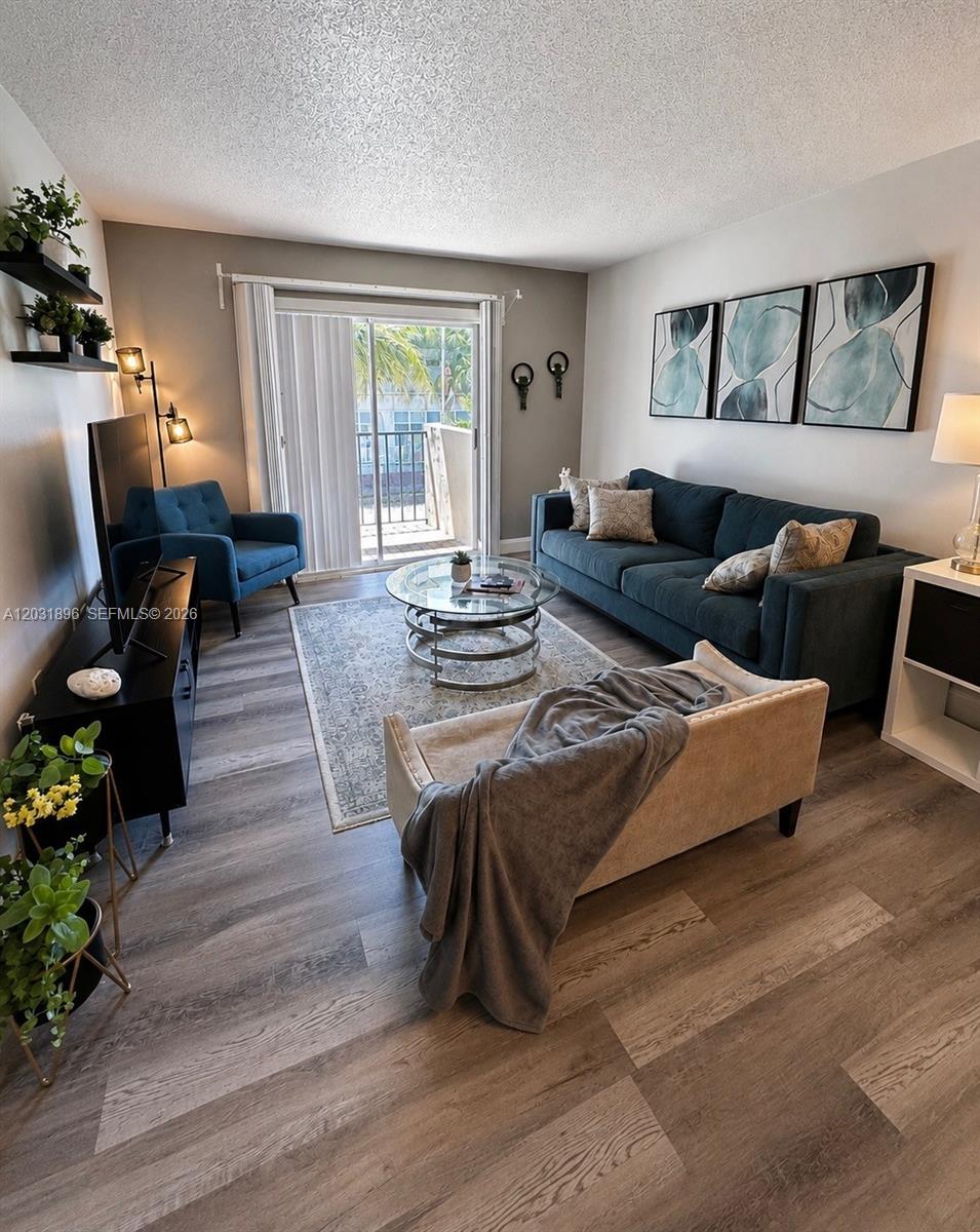 A living room features a dark blue sofa, a glass coffee table, and wood-look flooring — 1150 Collins Ave # 204, Miami Beach FL 33139, MIAMI BEACH, FL