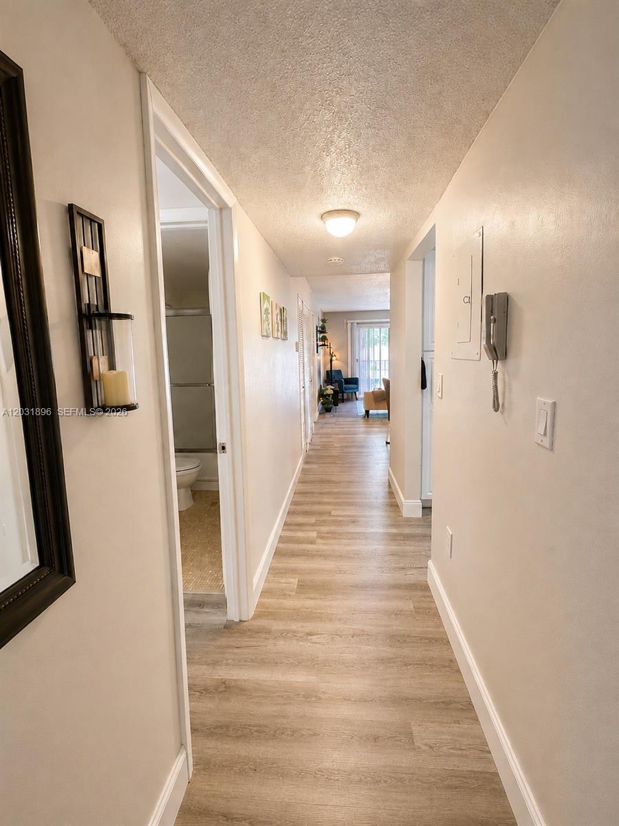 A hallway with light wood-look flooring leads toward a living area with a sliding door — 1150 Collins Ave # 204, Miami Beach FL 33139, MIAMI BEACH, FL