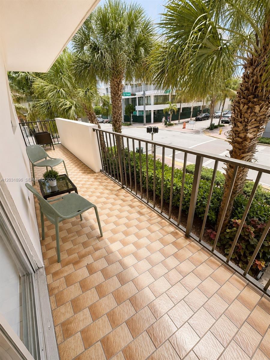 A balcony with tiled flooring, two green chairs, a small table, and palm trees — 1150 Collins Ave # 204, Miami Beach FL 33139, MIAMI BEACH, FL
