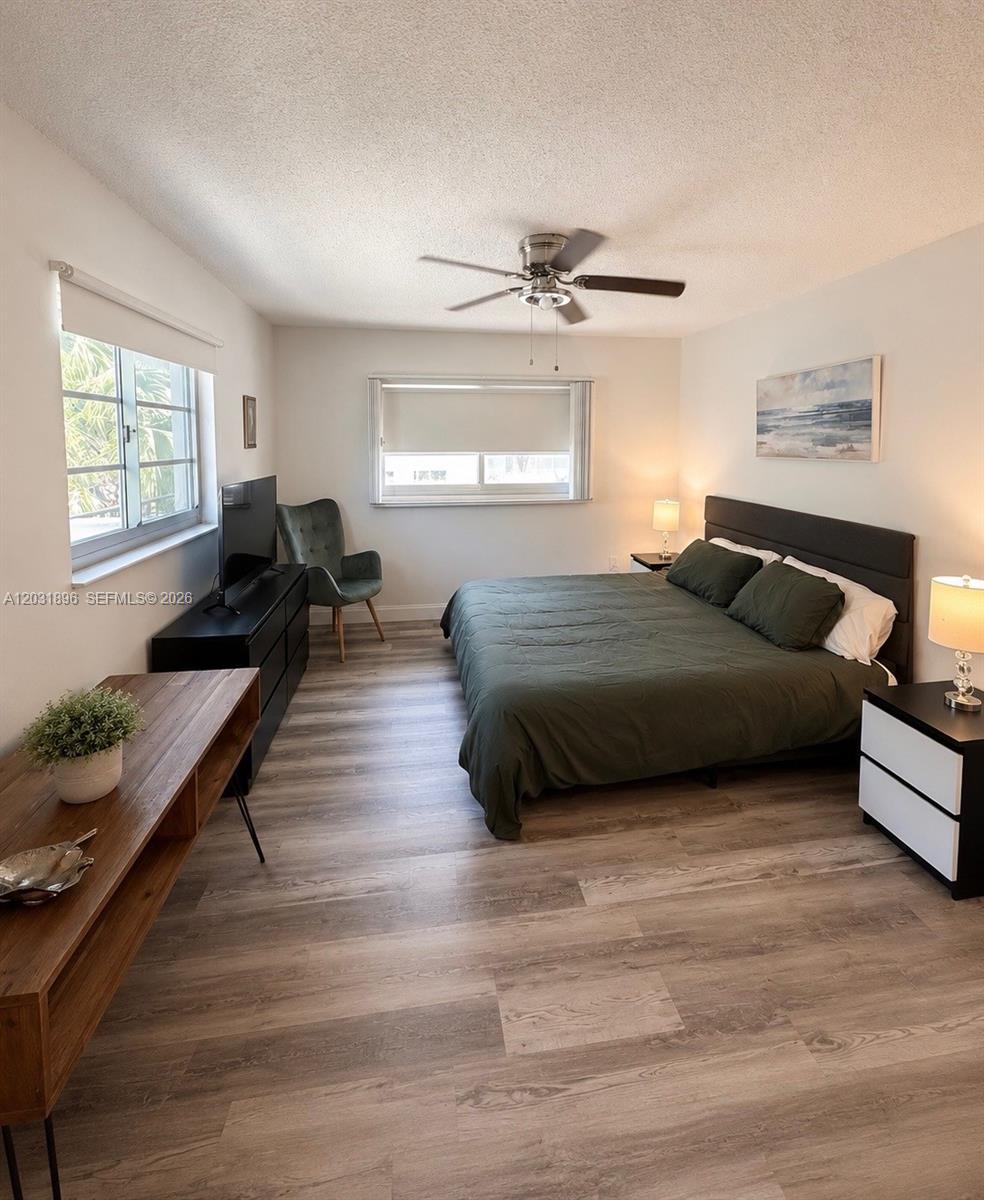 A bedroom features a bed with a green comforter, wood-look flooring, and a ceiling fan — 1150 Collins Ave # 204, Miami Beach FL 33139, MIAMI BEACH, FL