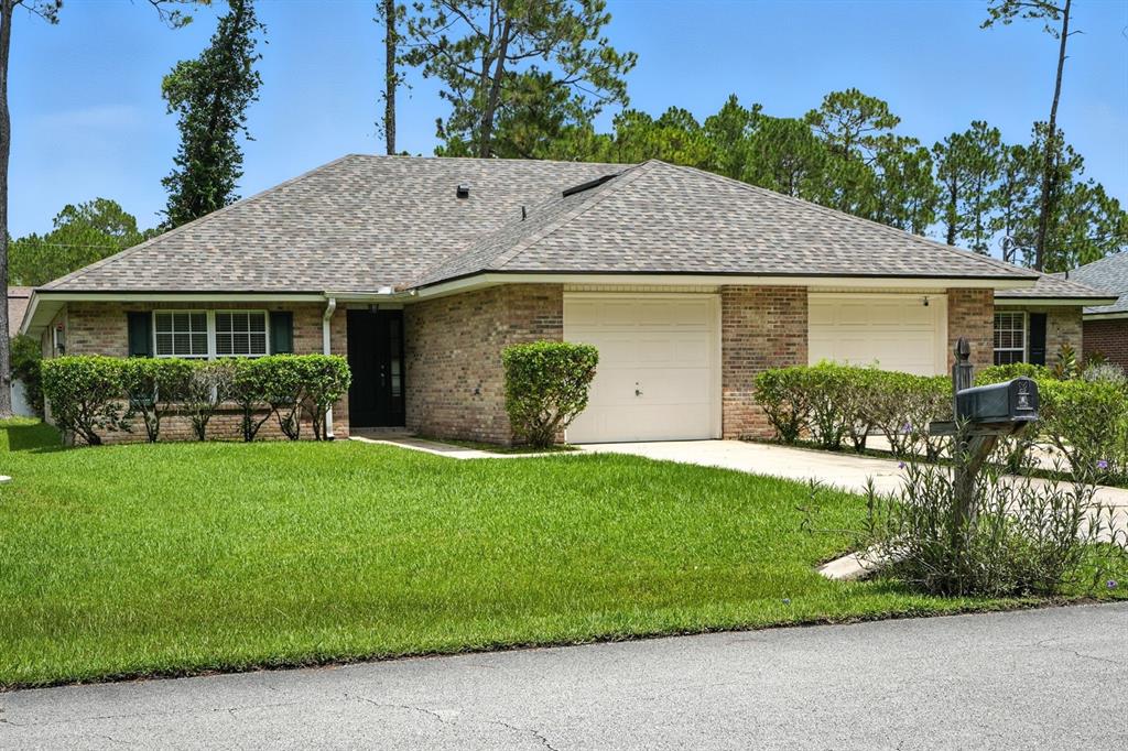 A single-story brick duplex with two garage doors and a manicured front lawn — 70 RED MILL DRIVE, PALM COAST, FL