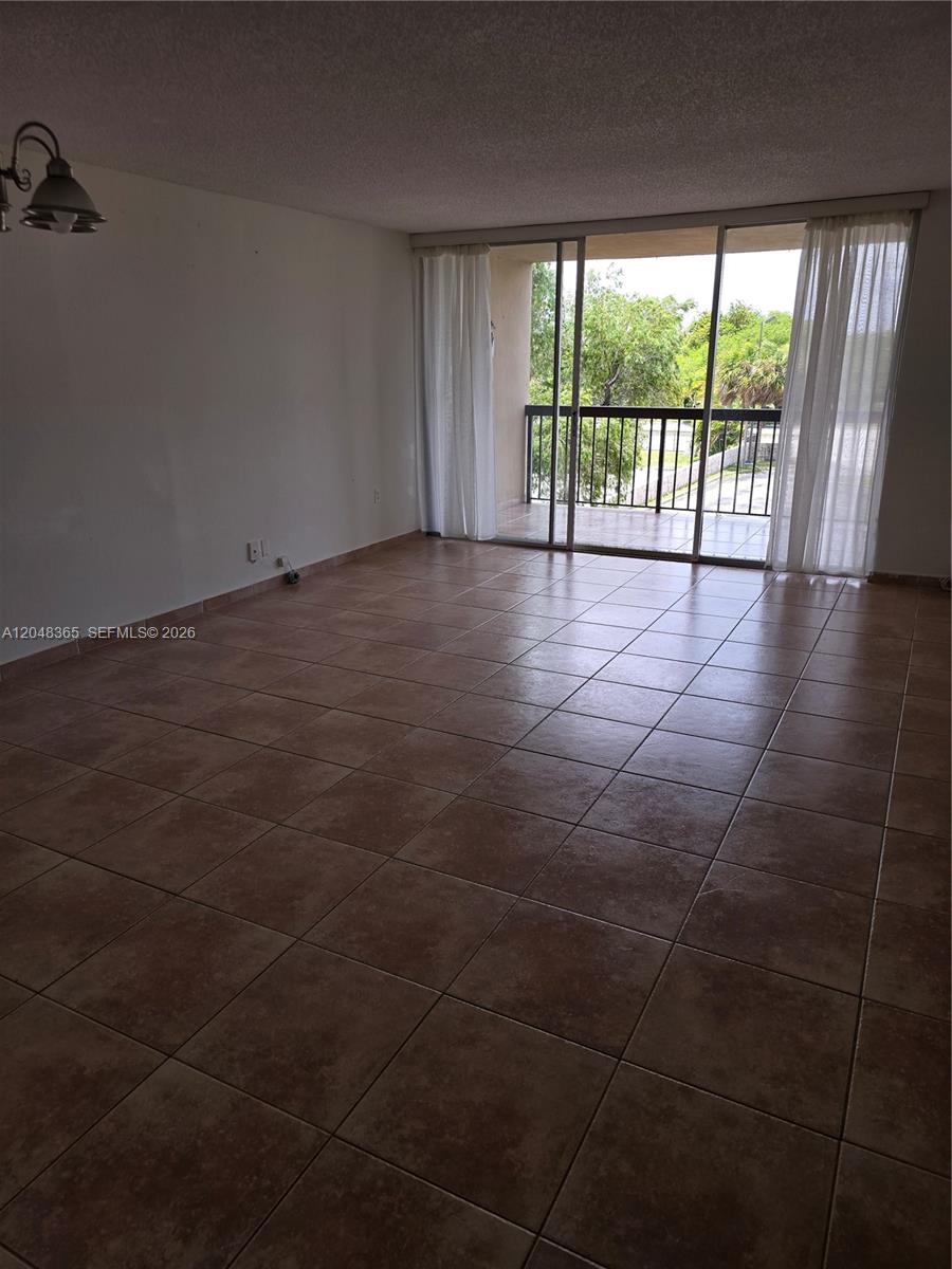An empty room features brown tile flooring, white walls, and a sliding glass door to a balcony — 5800 SW 127th Ave # 2310, Miami FL 33183, MIAMI, FL