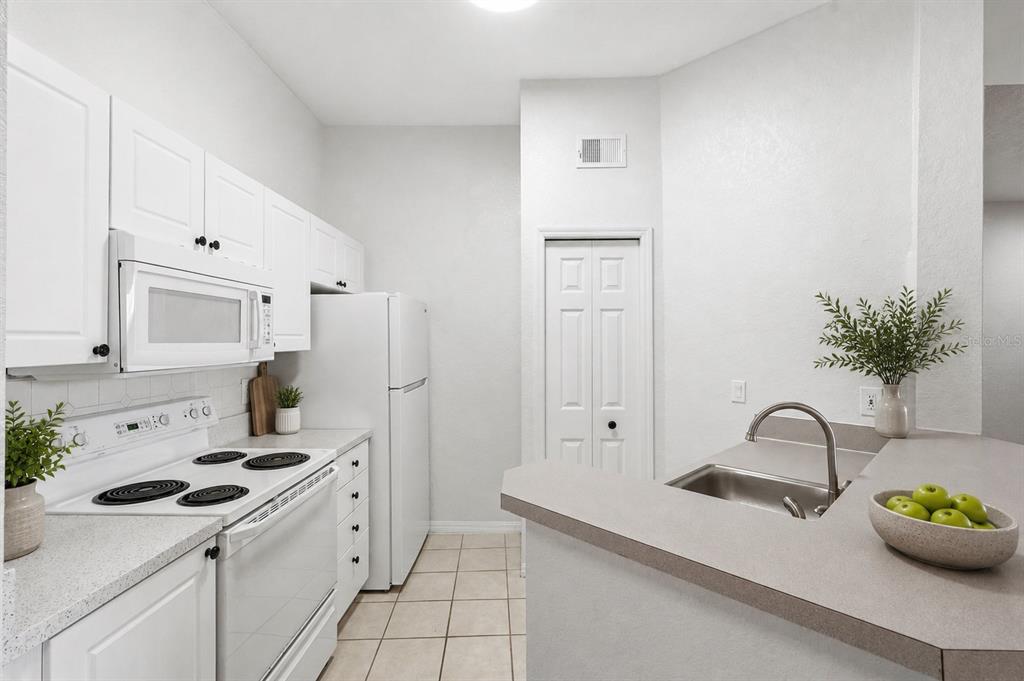A kitchen features white cabinets, white appliances, tile flooring, and a peninsula with a sink — 18106 PEREGRINES PERCH PLACE UNIT 5302, LUTZ, FL