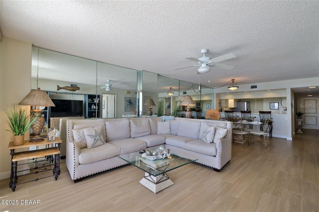 A living room features a large sectional sofa, mirrored walls, and a glass coffee table — 3855 S ATLANTIC AVENUE UNIT 1405, DAYTONA BEACH, FL