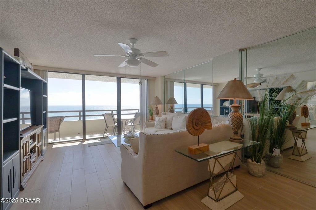 A living room features light wood flooring, a beige sofa, and a balcony overlooking the ocean — 3855 S ATLANTIC AVENUE UNIT 1405, DAYTONA BEACH, FL