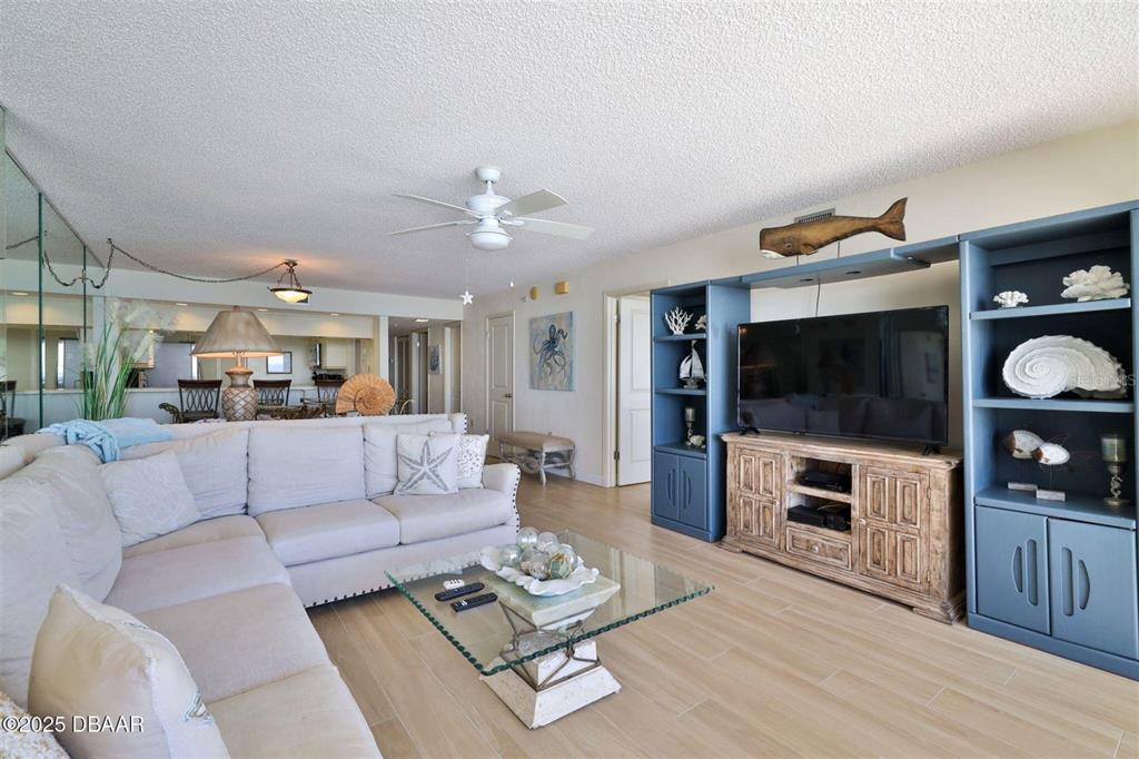 A living room features a sectional sofa, a glass coffee table, and blue built-in shelving — 3855 S ATLANTIC AVENUE UNIT 1405, DAYTONA BEACH, FL