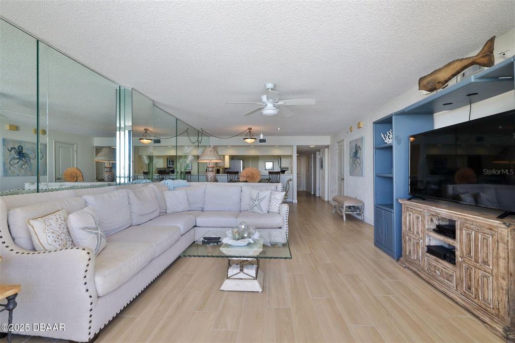 A living room features a large sectional sofa, mirrored walls, and a wooden media console — 3855 S ATLANTIC AVENUE UNIT 1405, DAYTONA BEACH, FL