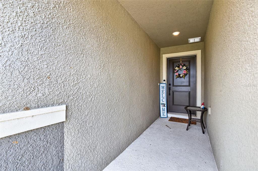 A covered entryway features a dark front door, a welcome sign, and a small table — 9972 MESIC WOODS AVENUE, SEFFNER, FL