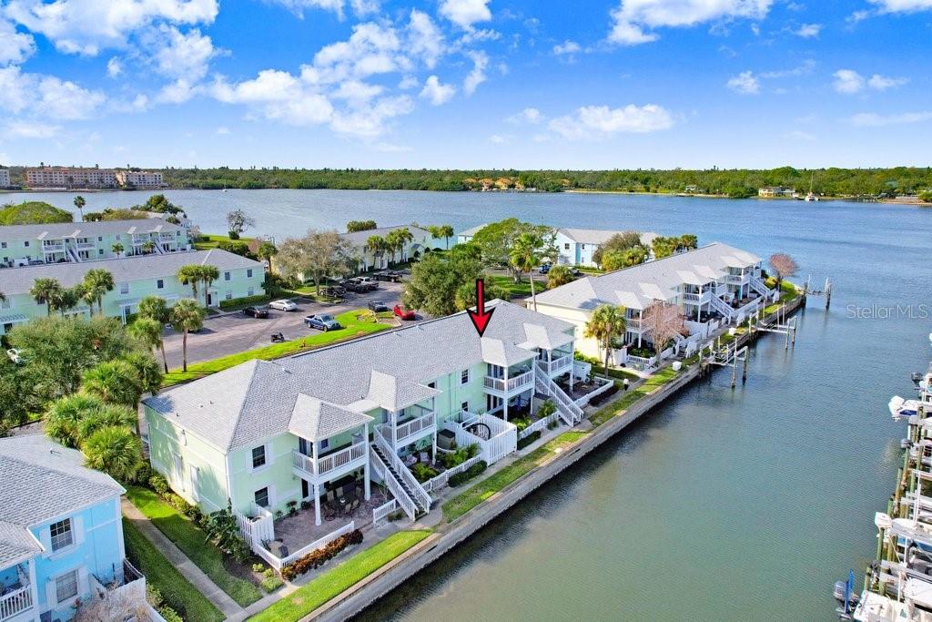 An aerial view shows a light green waterfront condominium building with a red arrow pointing down — 5012 STARFISH DRIVE SE UNIT B, ST PETERSBURG, FL