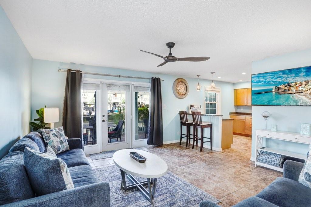 A living room with a blue sofa, coffee table, ceiling fan, and an open kitchen area — 5012 STARFISH DRIVE SE UNIT B, ST PETERSBURG, FL