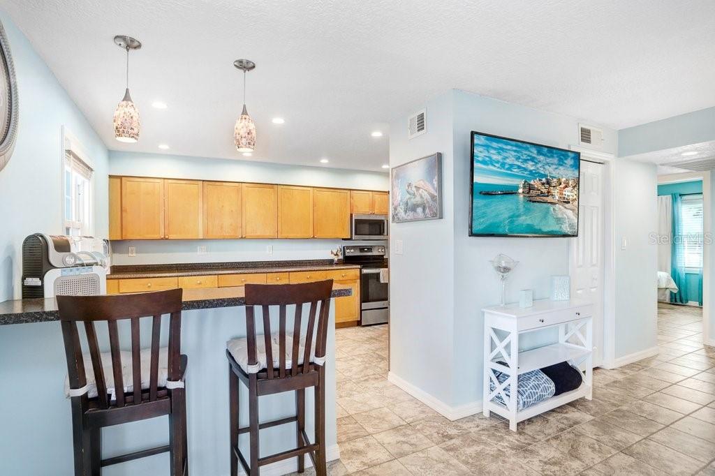A kitchen with light wood cabinets and a breakfast bar overlooks a tiled living area — 5012 STARFISH DRIVE SE UNIT B, ST PETERSBURG, FL